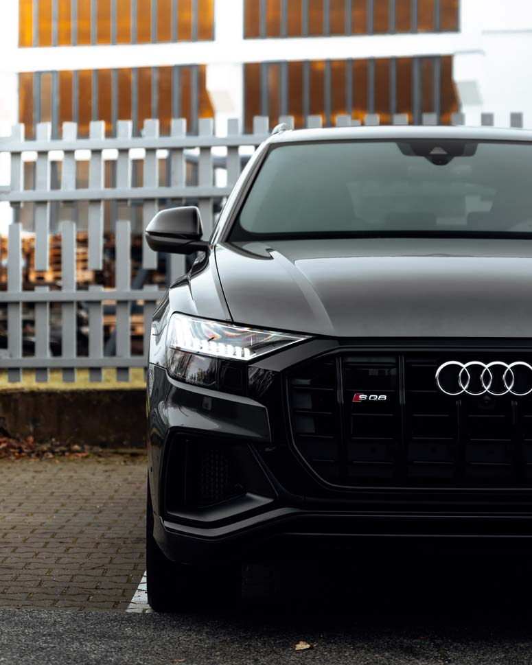 A black audi q8 is parked in front of a fence.