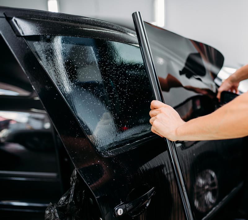 A person is applying window tinting to a black car.