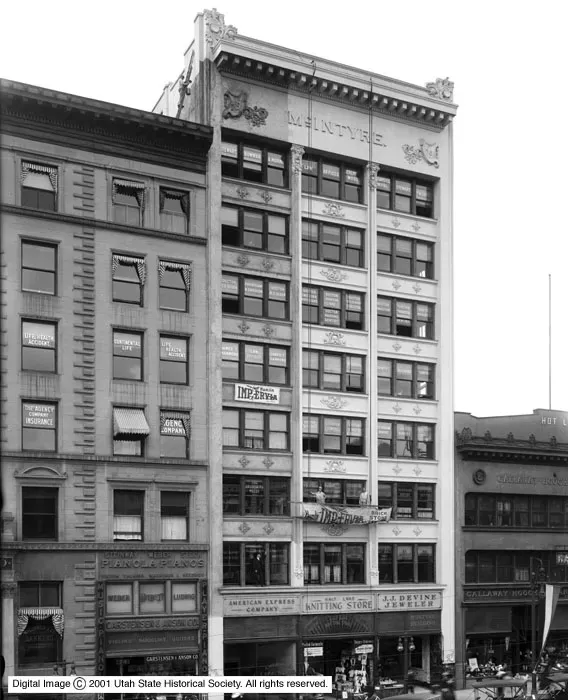 A black-and-white historic street view of three adjacent commercial buildings in a city with architectural detailing.