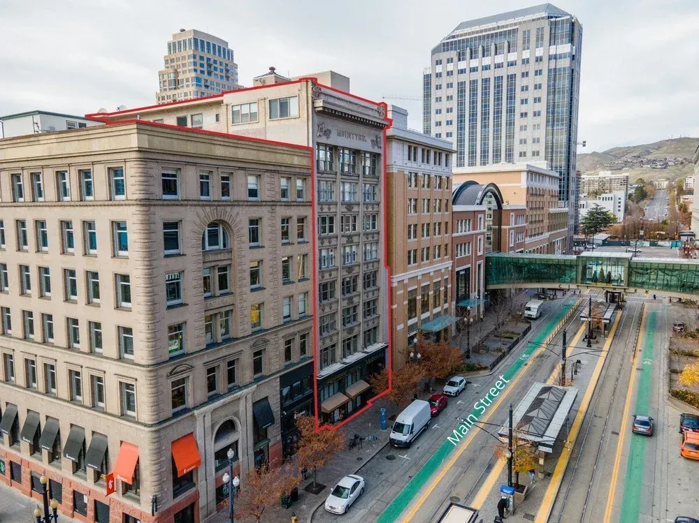 A high-angle view of city buildings with an orange outline highlighting a multi-story building along a street with tracks.
