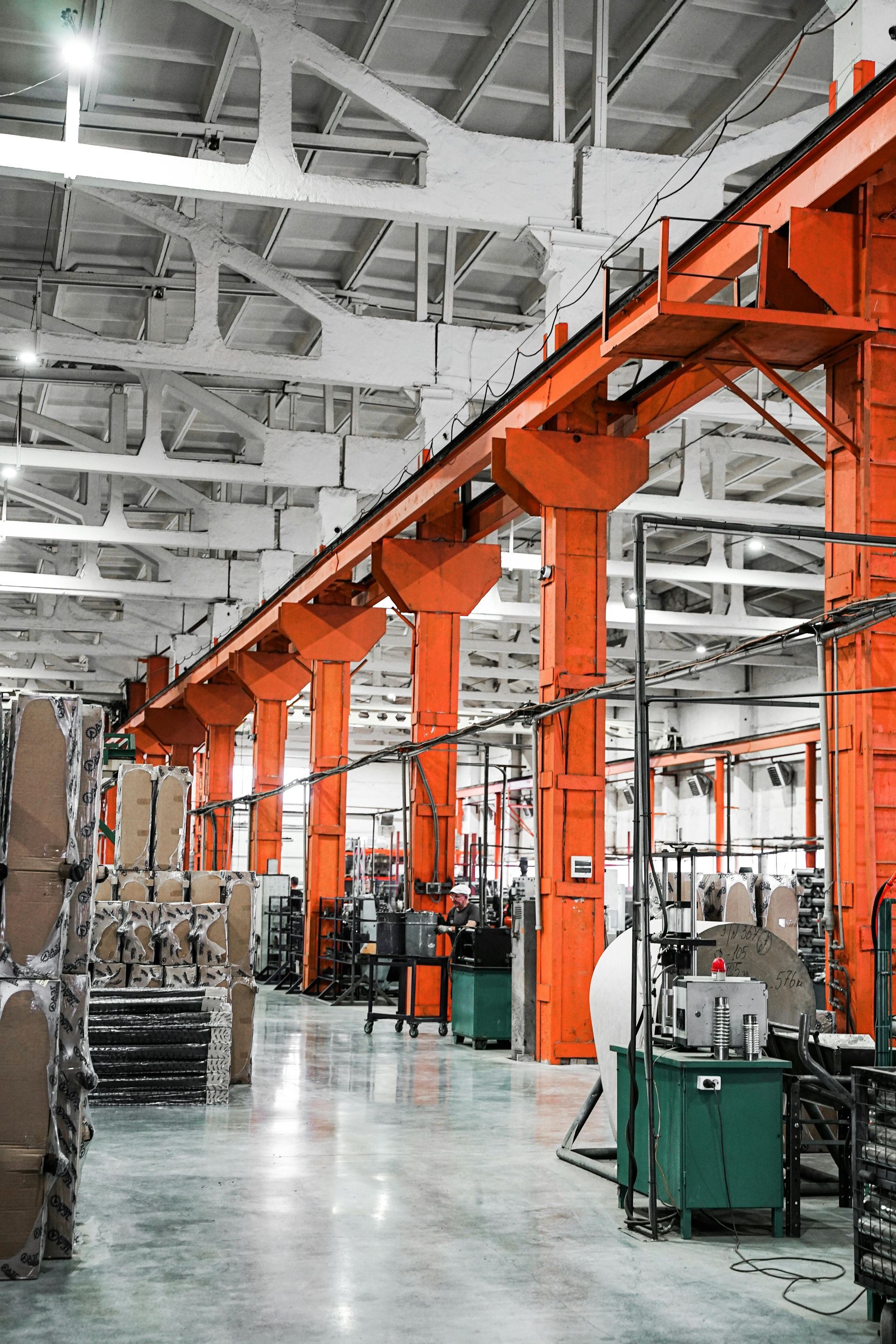 Orange industrial supports in a factory, with machinery, boxes, and teal cabinets.