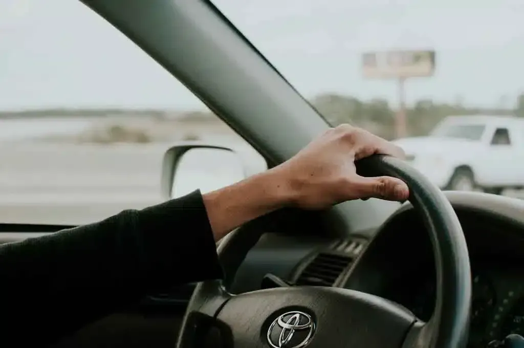Hand on steering wheel inside a car on a highway, with a white vehicle passing outside the window