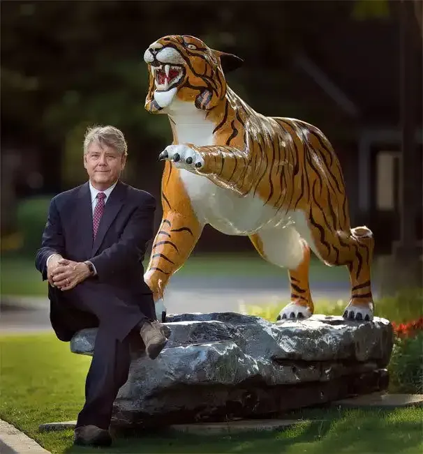 Man seated beside a tiger statue on a rock in a garden setting