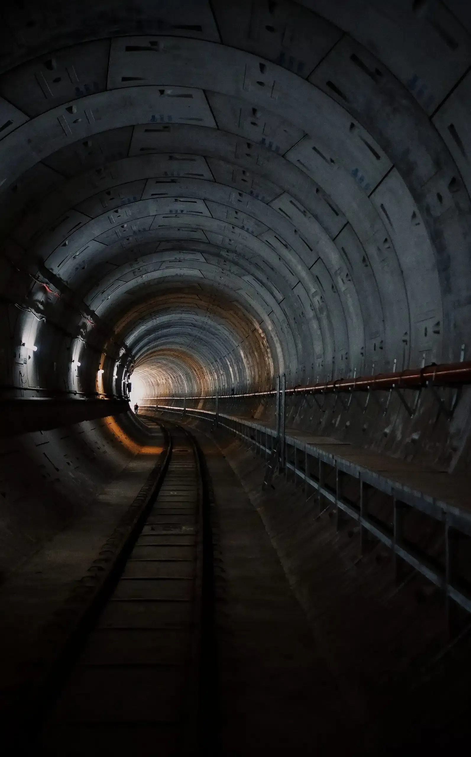 Dark tunnel with railway tracks curving toward a bright opening