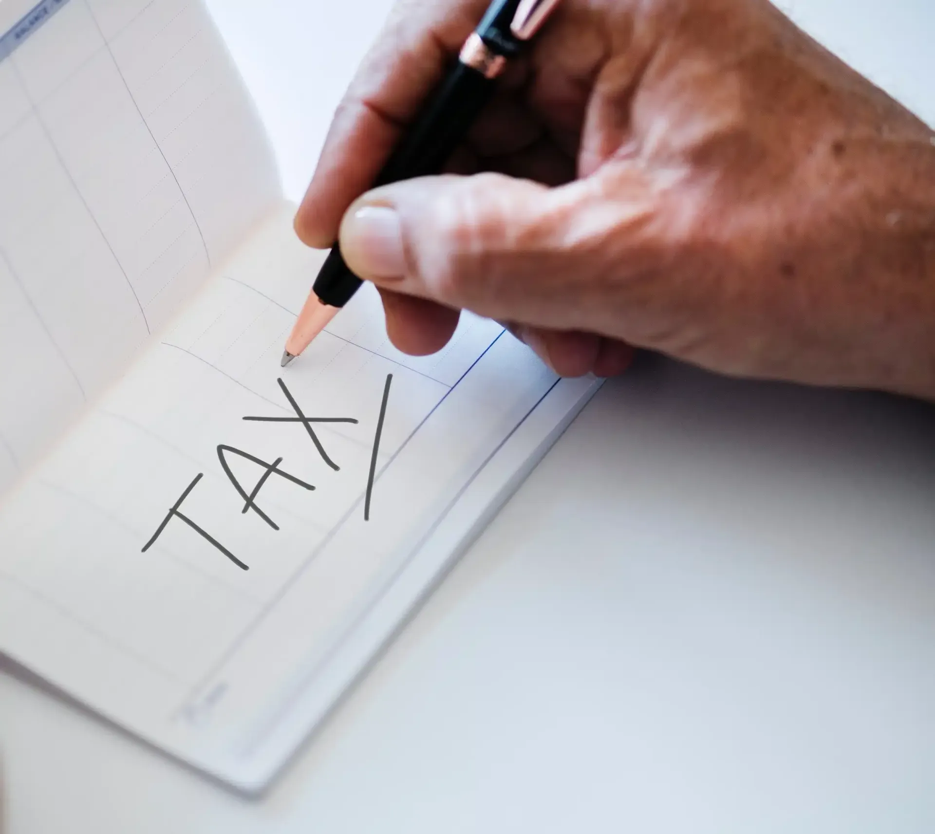 Hand writing “TAX” on a notepad with a pencil.
