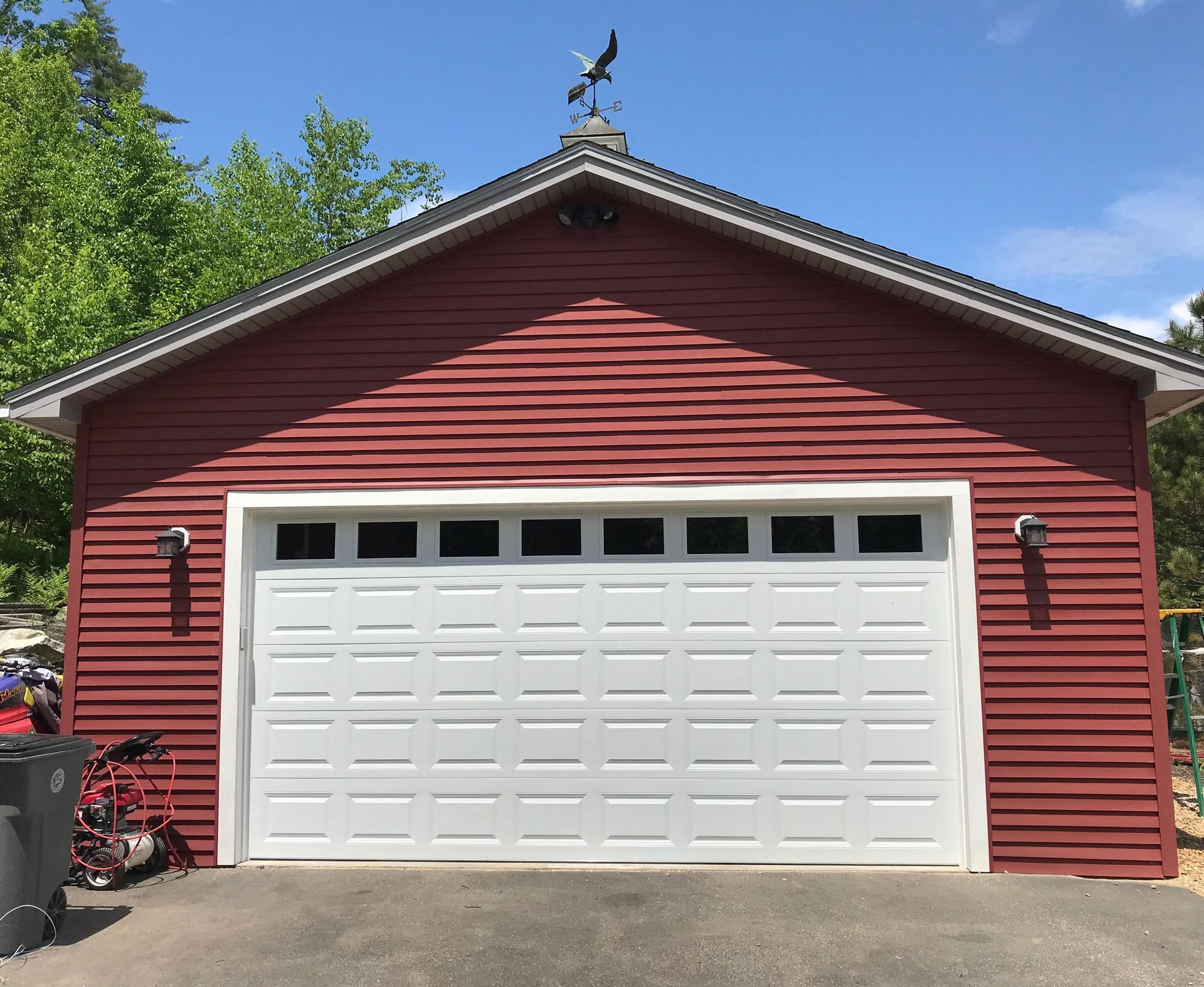 Red garage with white door and eagle weathervane against blue sky.