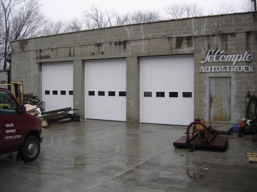 Exterior of a garage with three closed white doors and a sign that reads 