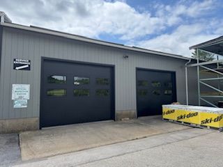 Two garage bays with black doors; exterior is gray, concrete slab in front.