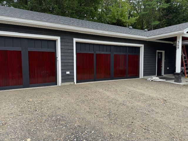 Gray house with red-tinted garage doors. Gravel driveway in front.