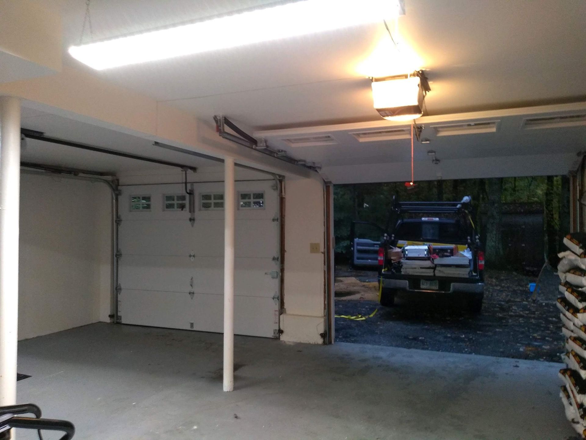 An open garage with a white door, concrete floor, and a vehicle parked outside.