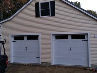 Two-car garage with white doors, black hardware, and beige siding. Small window with black shutters above.