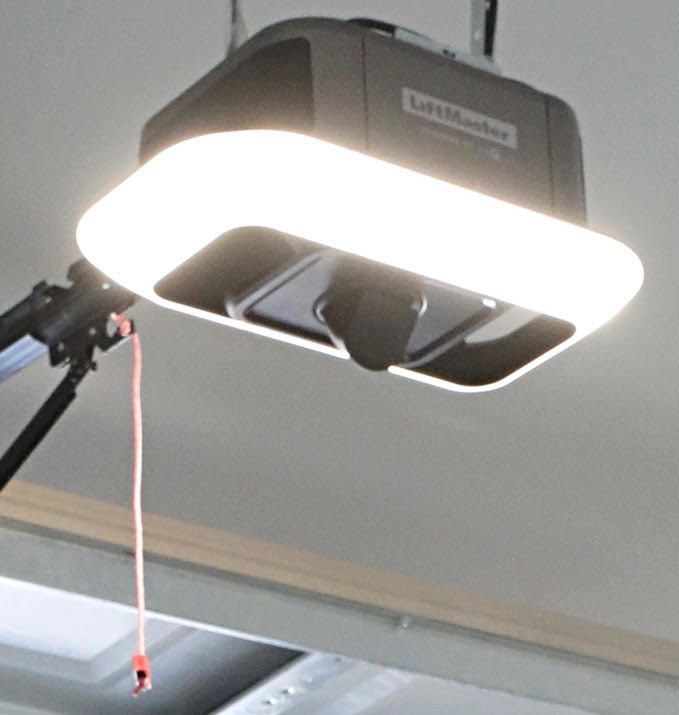 A LiftMaster garage door opener with a bright, white light illuminating the garage ceiling.