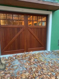 Wooden garage door with glass windows, diagonal accents. Brown wood, white trim, construction site.