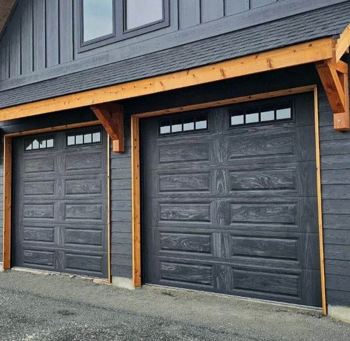 Two dark gray garage doors with small glass windows, set in a wood-trimmed building.