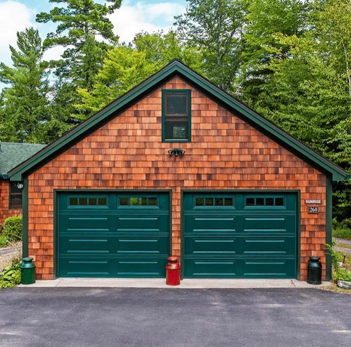 Two-car garage with green doors and cedar shake siding. Set in a wooded area, with matching green trim.