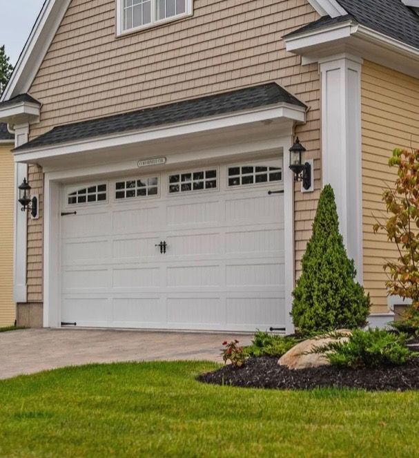 White garage door on a tan house with a manicured lawn.