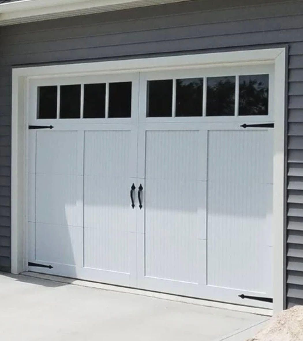 White garage door with window panels and black hardware, set against gray siding.