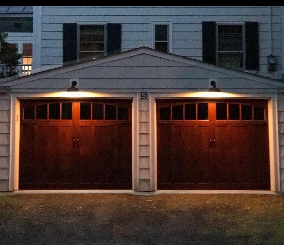 Two dark wooden garage doors with lights above them, on a light-colored building at night.