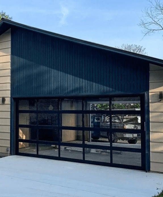 Garage with glass door, black frame, blue siding, and beige wall. Concrete driveway.