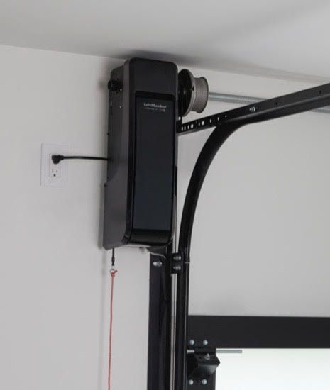 Black garage door opener mounted on a white wall, attached to a curved black track. Red emergency cord hangs down.