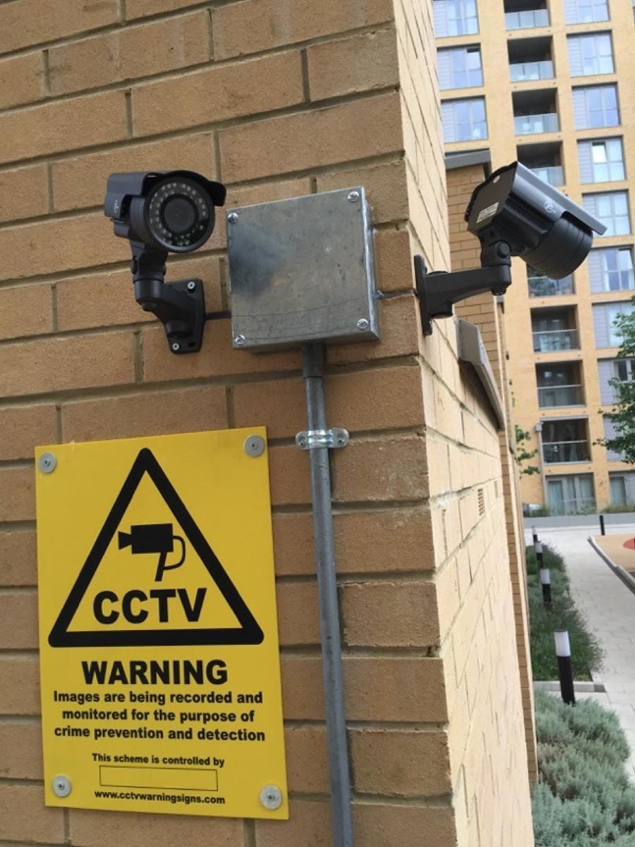two security cameras are mounted on a brick wall next to a warning sign
