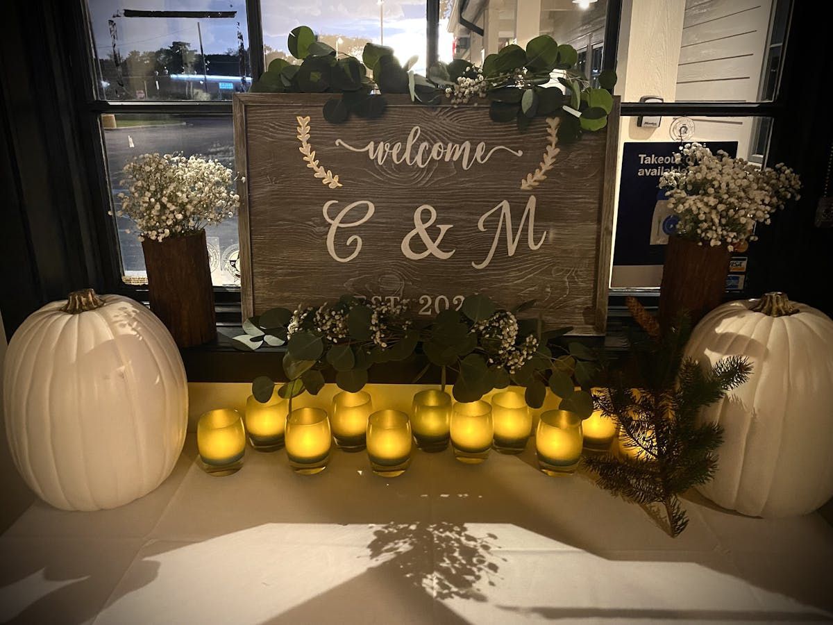 A wooden sign that says welcome c & m is on a table with pumpkins and candles.