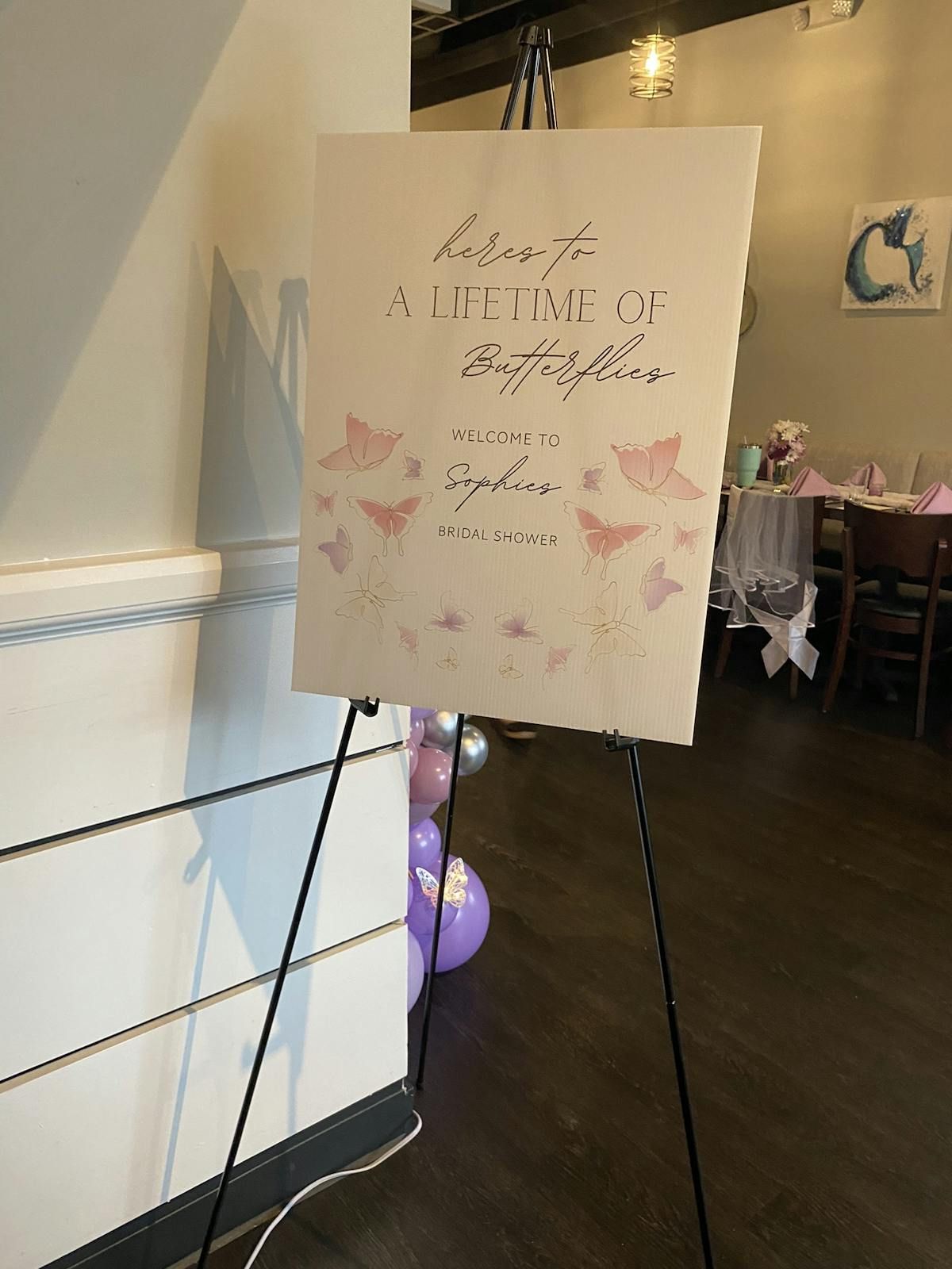 A sign on an easel in a room with purple balloons