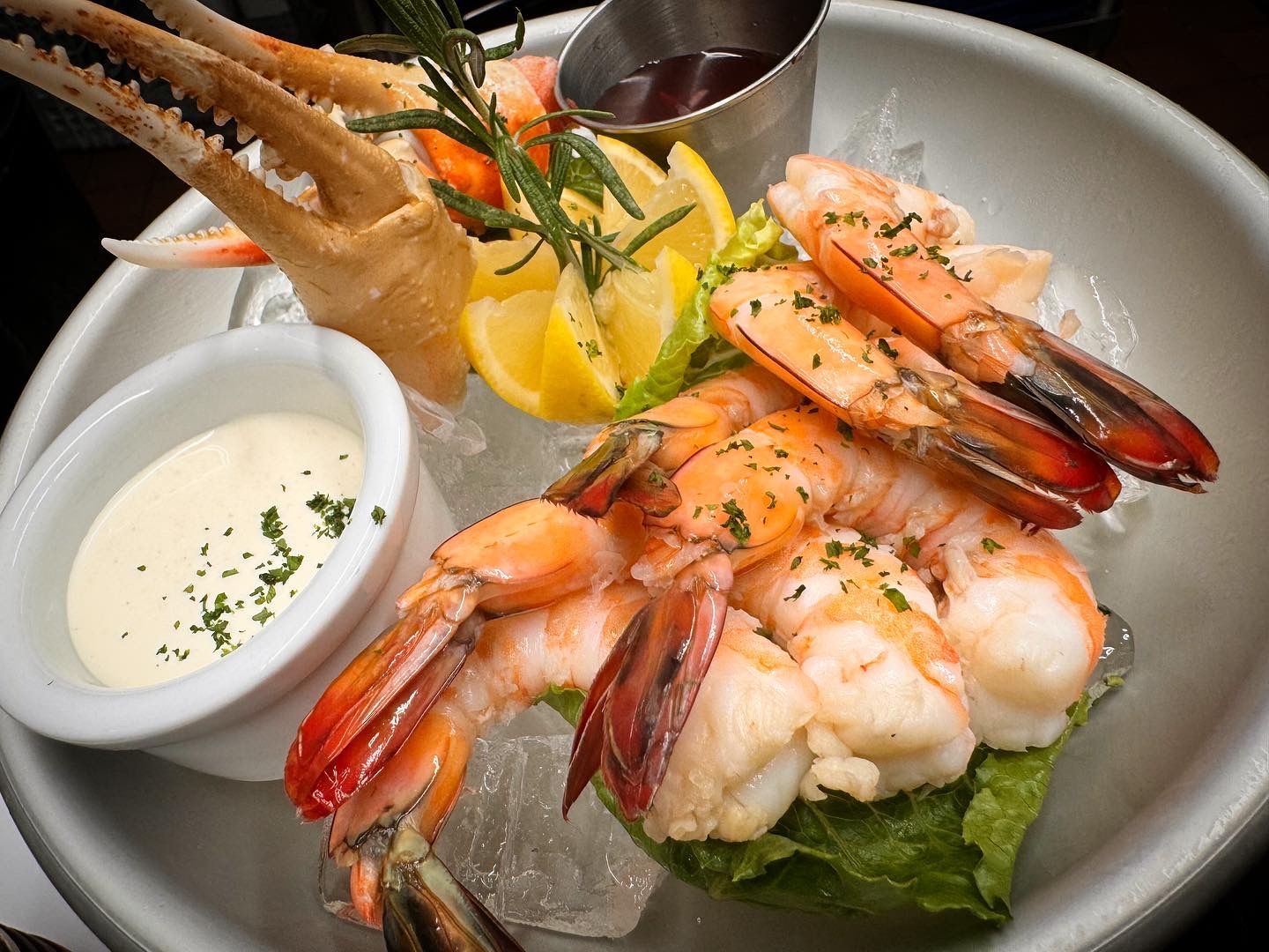 A plate of shrimp and crab claws on ice with a dipping sauce.