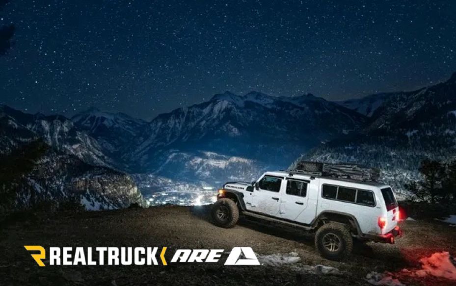 White truck on a mountain road at night, with starry sky and logo for RealTruck ARE.