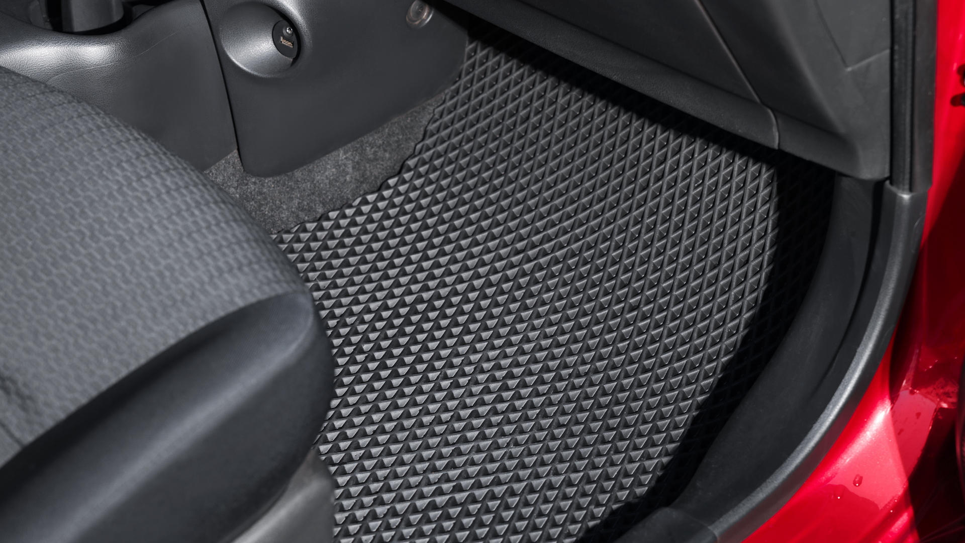 Black rubber car floor mat with a geometric pattern, inside a red car.