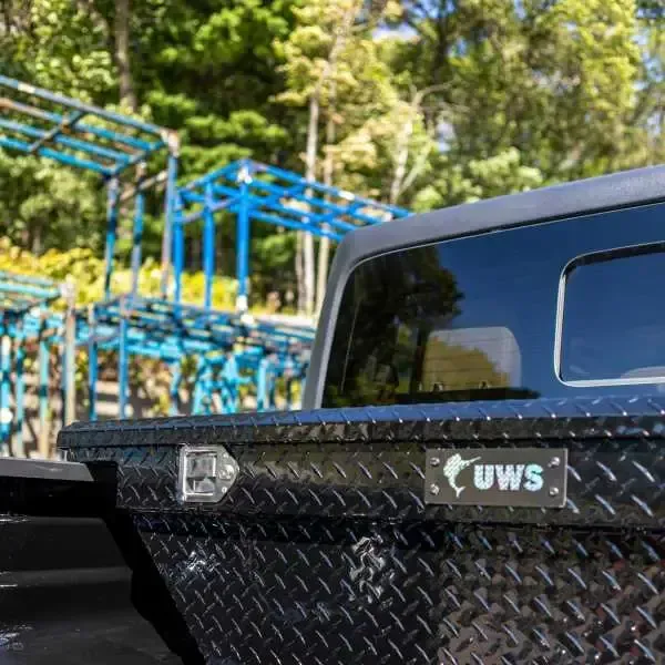Black diamond-plated UWS truck tool box installed on a pickup truck. Outdoors setting.