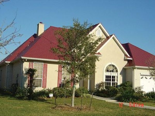 Tan stucco house with red roof, red shutters, and a small tree in front.