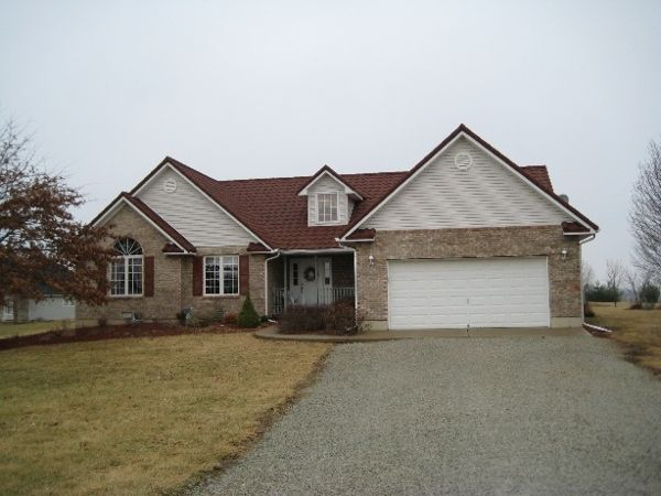 Tan brick house with red roof and white garage door. Driveway leads to the house on a cloudy day.