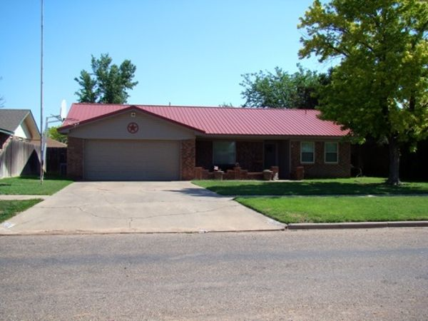 House with red metal roof, tan brick and garage, on a sunny day.