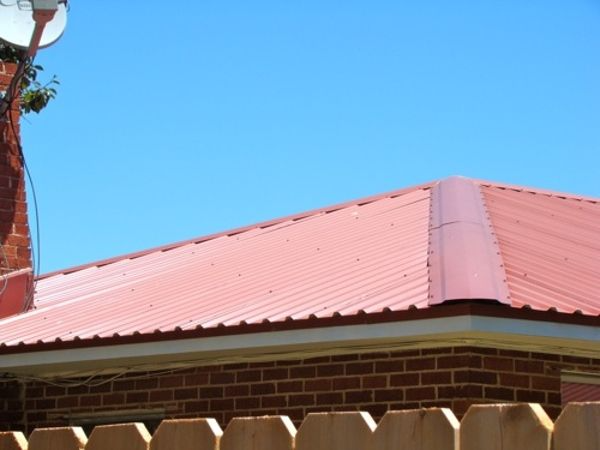 Red metal roof on a brick building with a blue sky background.