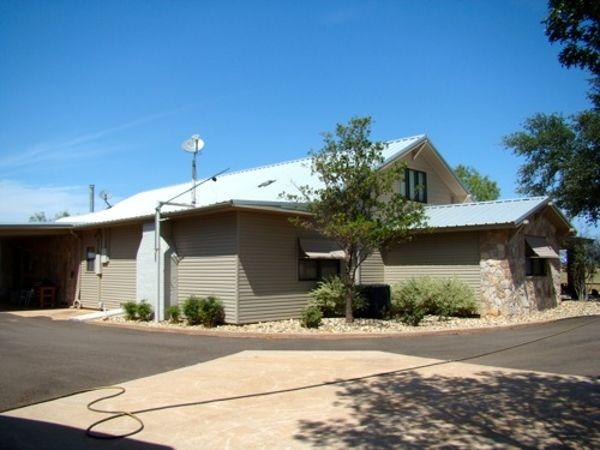 Tan house with metal roof, satellite dish, and driveway on a sunny day.