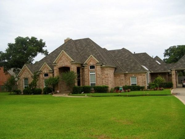 Brick house with a green lawn and a brown shingled roof under an overcast sky.