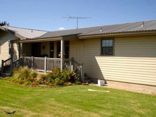 Tan house with a porch, metal roof, and antenna on a sunny day.