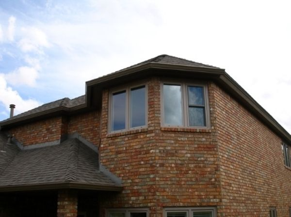 Brick house with multiple windows and a dark roof against a cloudy sky.