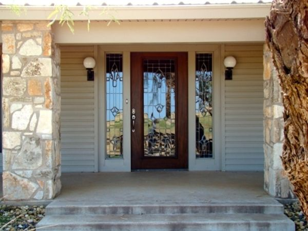 Beige house entry with stone columns, brown door, sidelights, and porch lights.