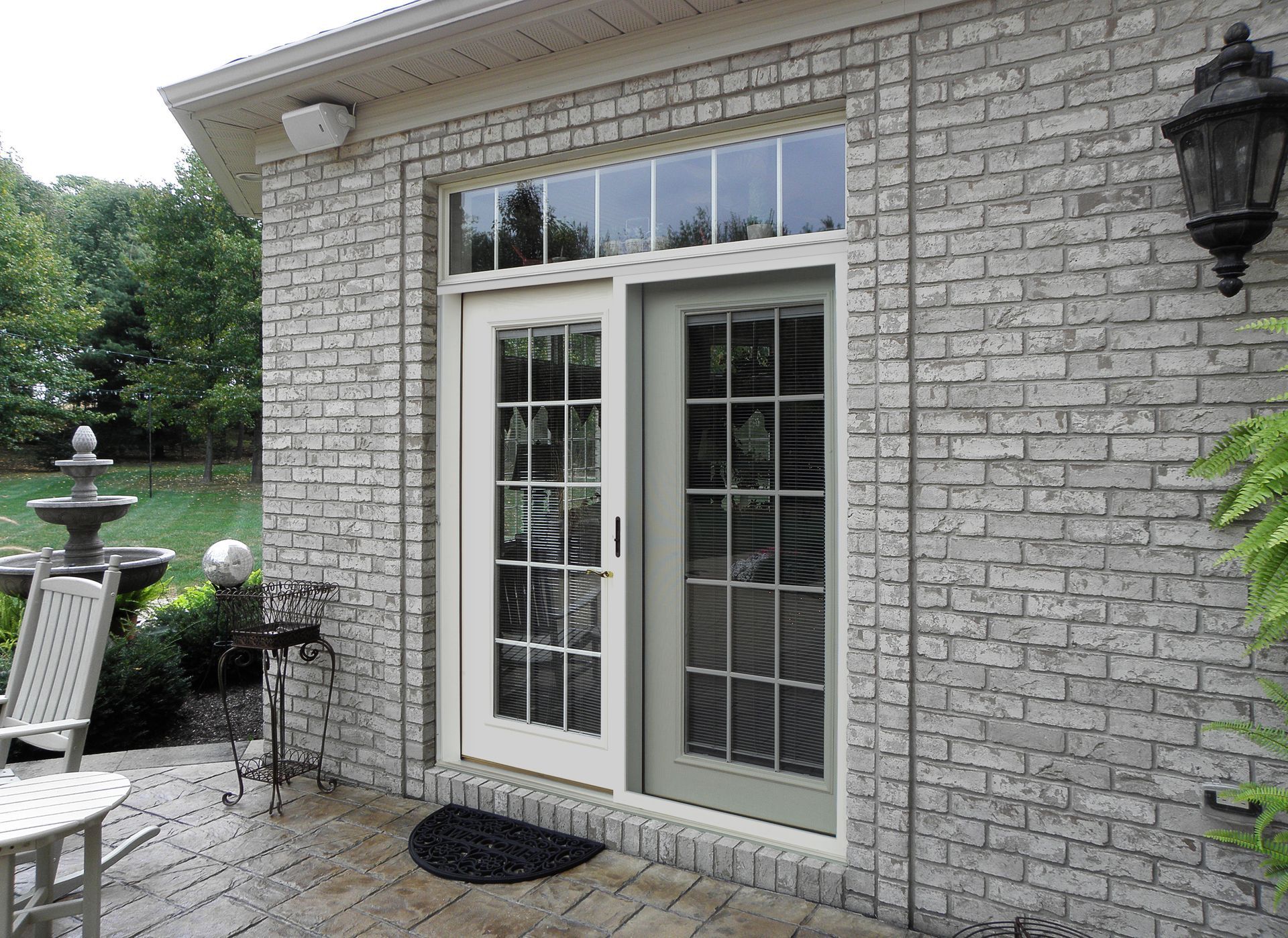 Brick wall with white framed glass door and window above, outdoor patio setting.