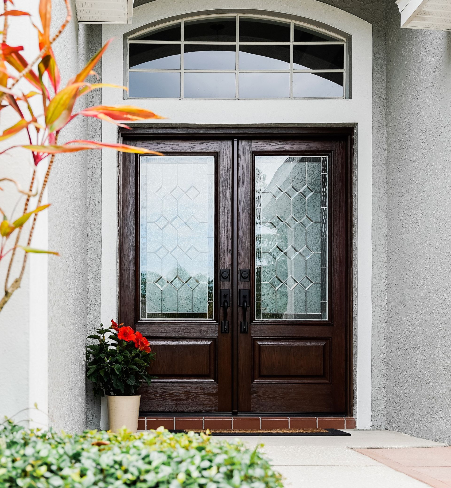 Dark brown double doors with glass panels and a decorative transom window above, set in a stucco facade.