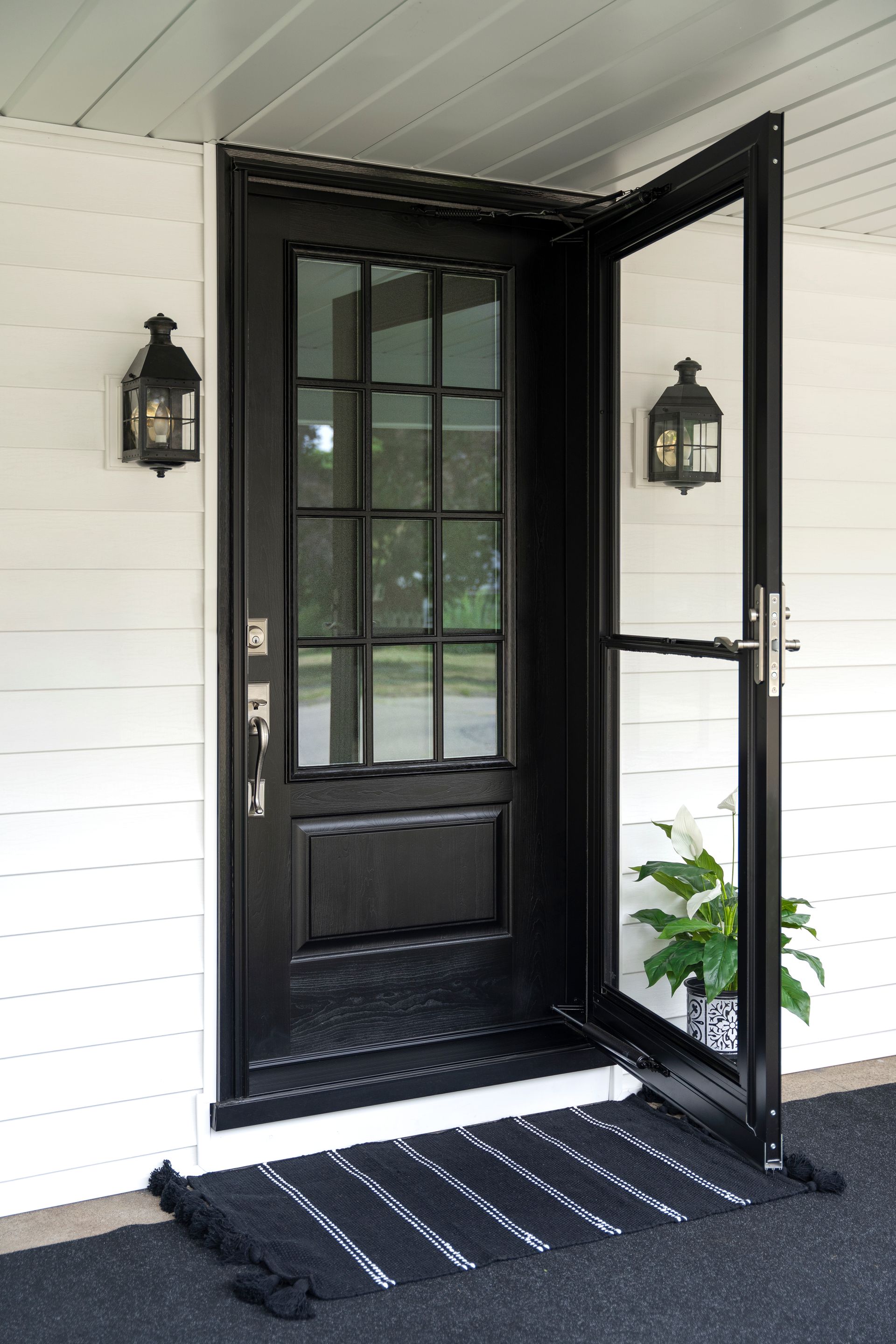Black front door with open screen door, lanterns, and a welcome mat.
