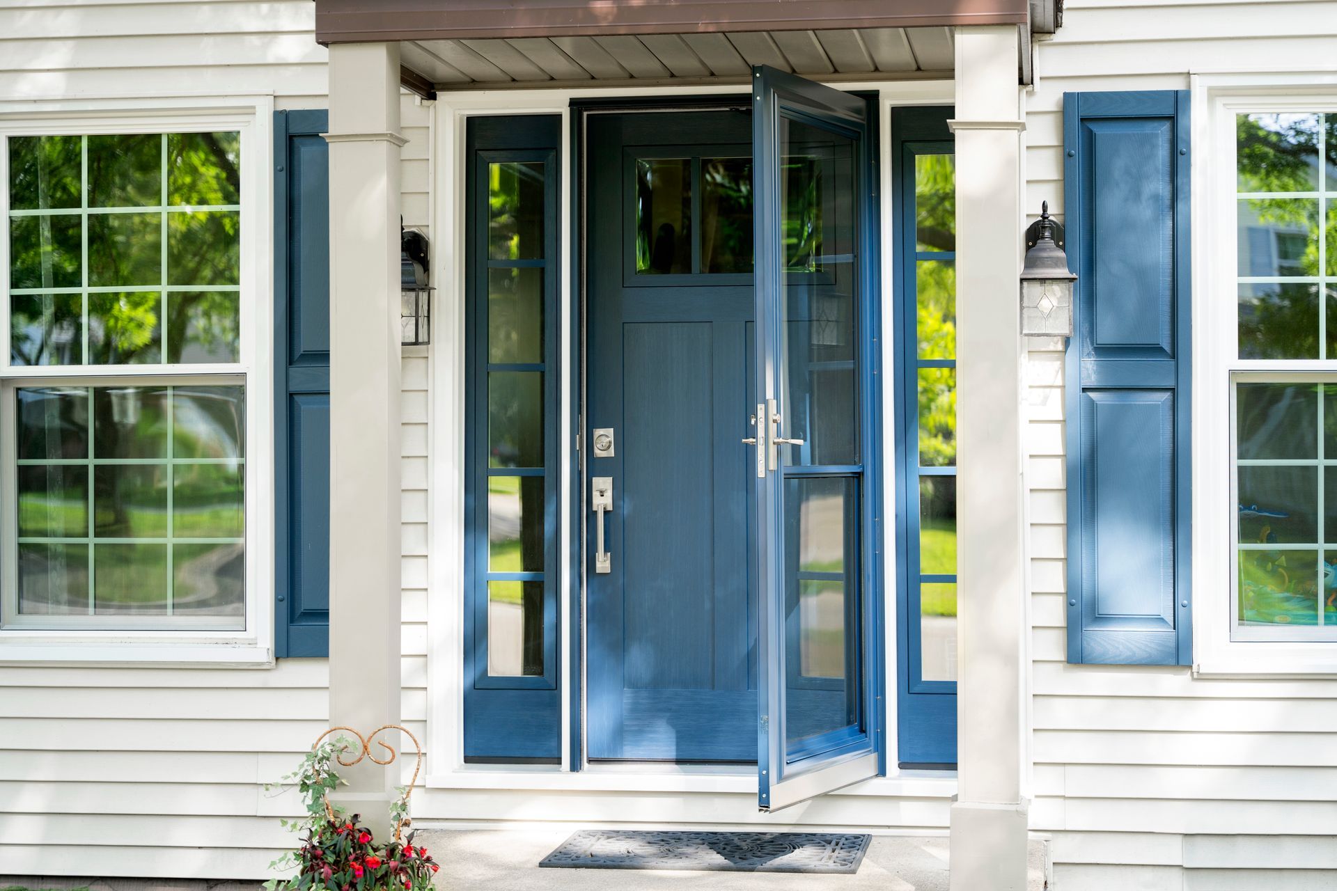 Blue front door with sidelights and screen door on a white house with blue shutters.