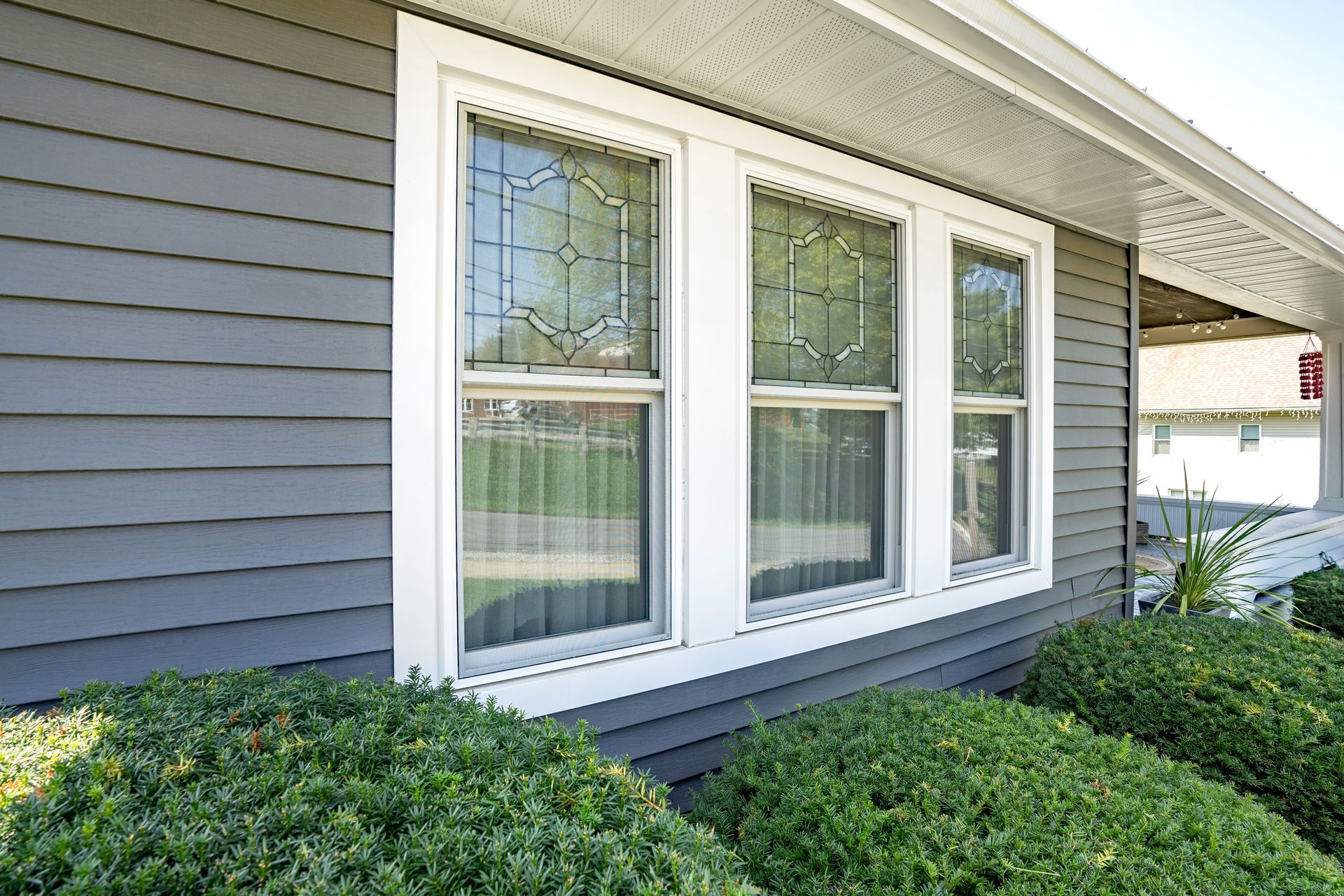 Gray house exterior with white-trimmed windows and green shrubs in front