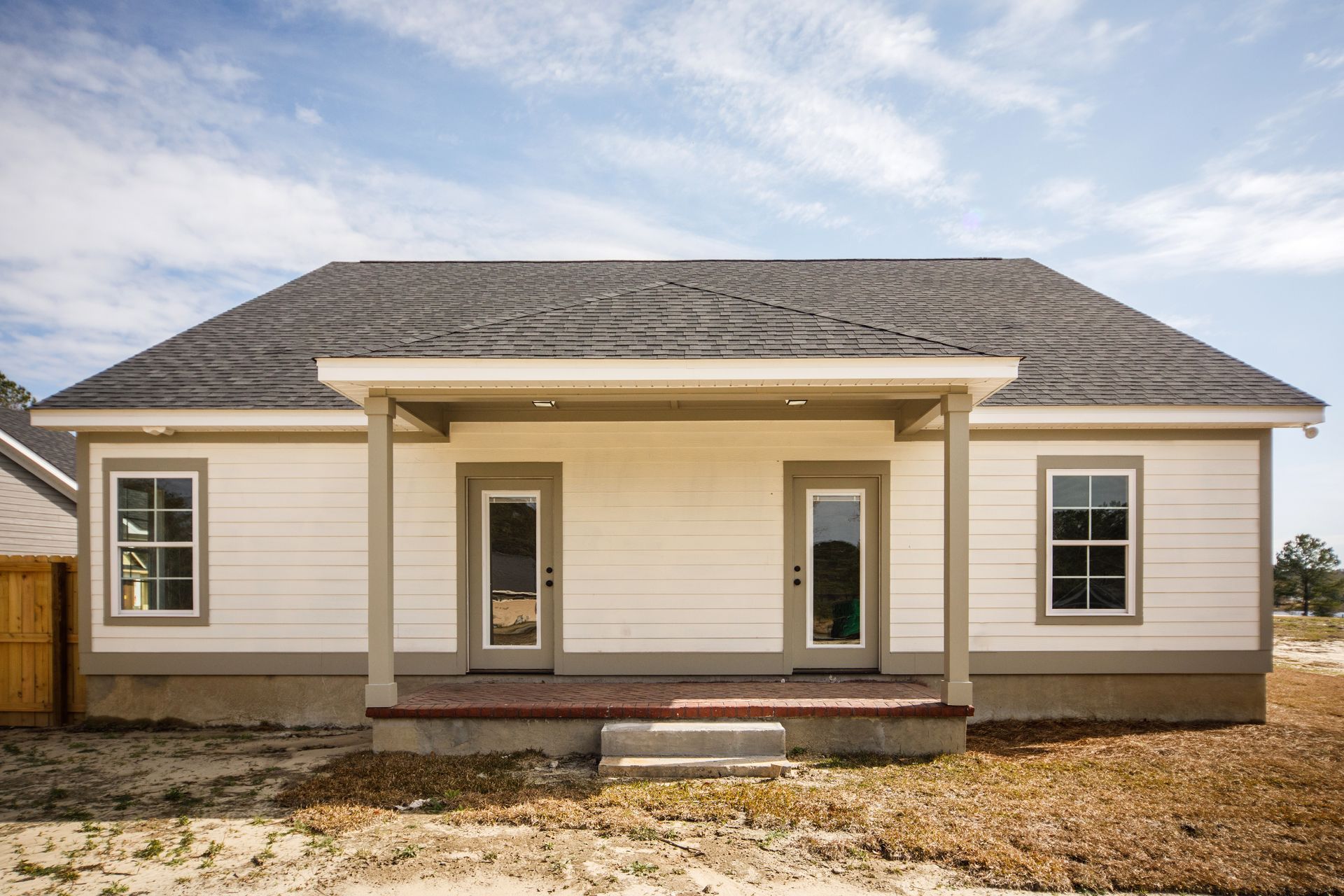 New single-story house with beige siding, gray shingle roof, and front porch under construction