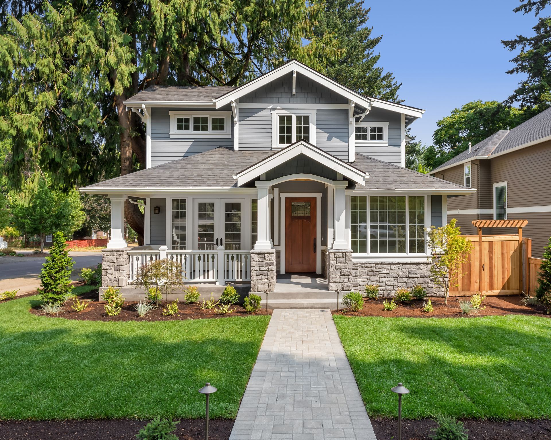 Two-story gray house with white trim, front porch, and a stone walkway across a green lawn