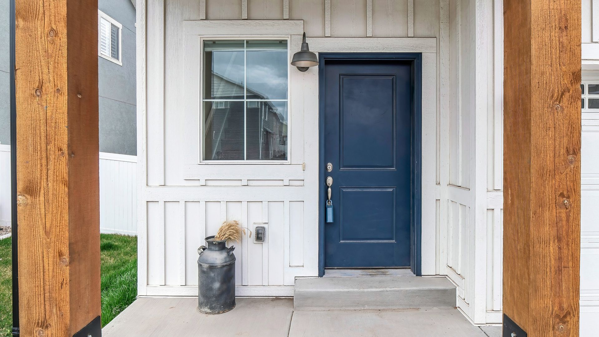 White front porch with a dark blue door, window, and a small trash can beside it.