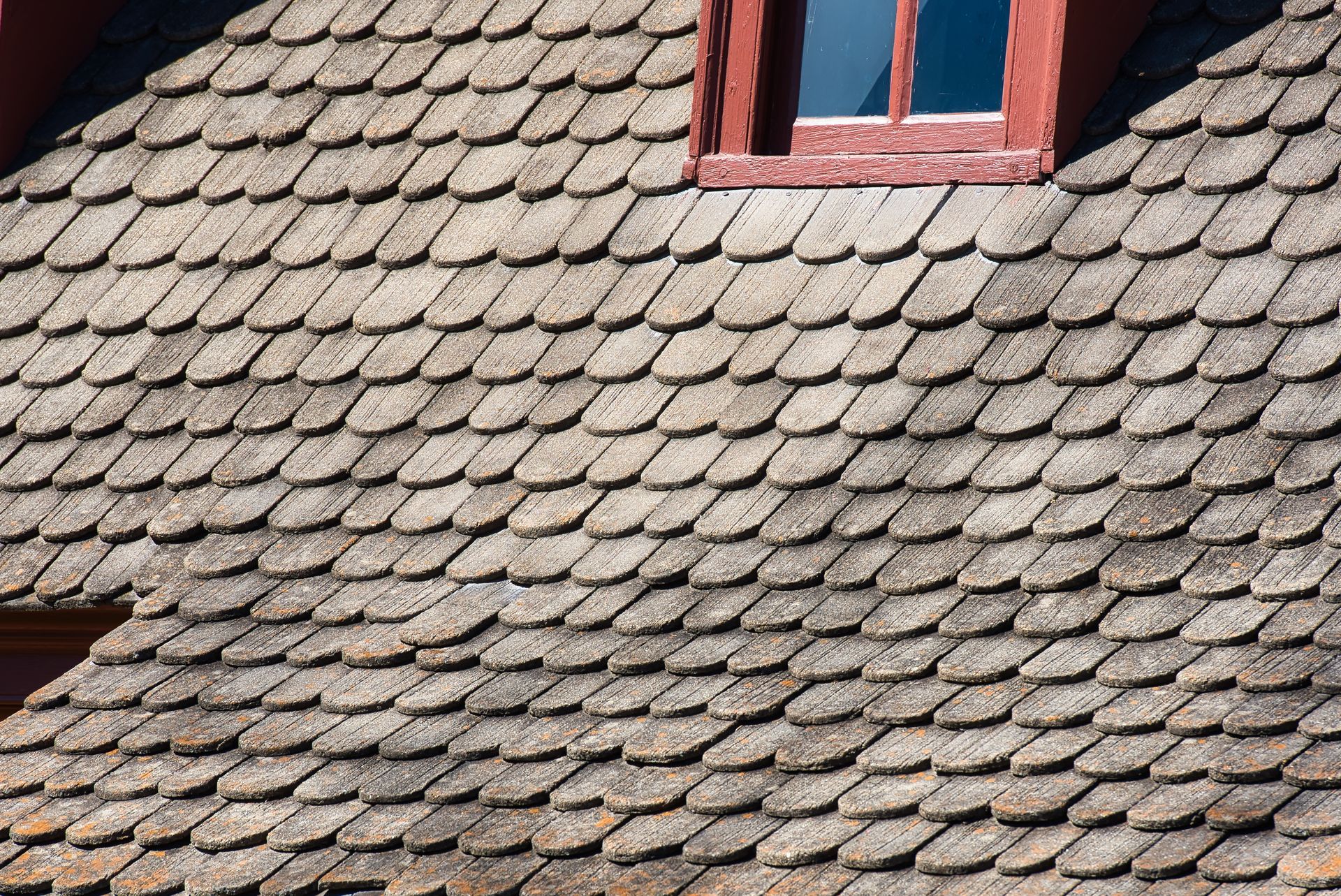 Red shingle roof with a small dormer window in sunlight