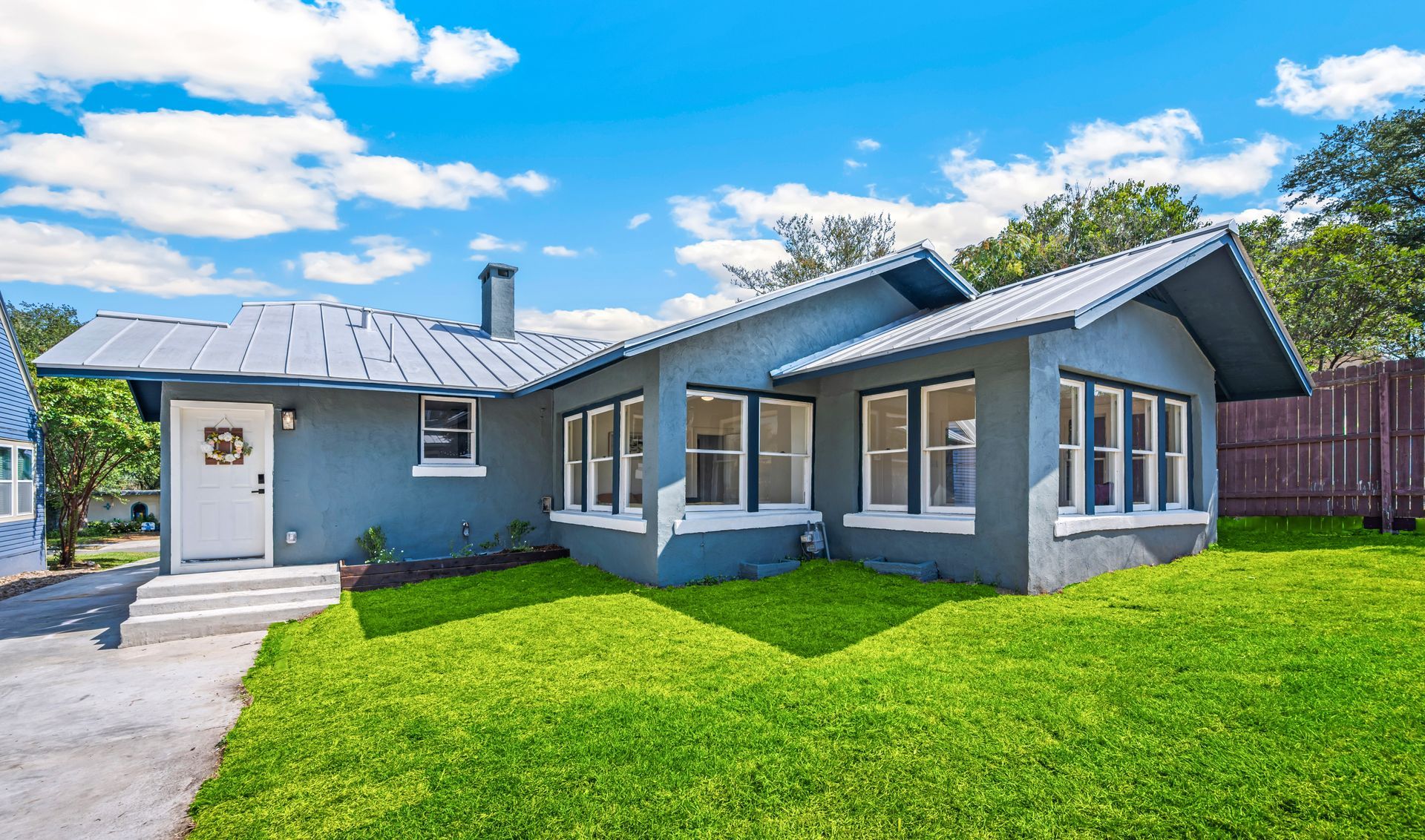 Modern gray house with large windows, green lawn, and driveway under a blue sky